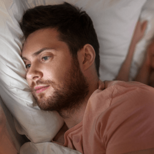 couple in bed and man looking at his mobile messages while woman sleeps