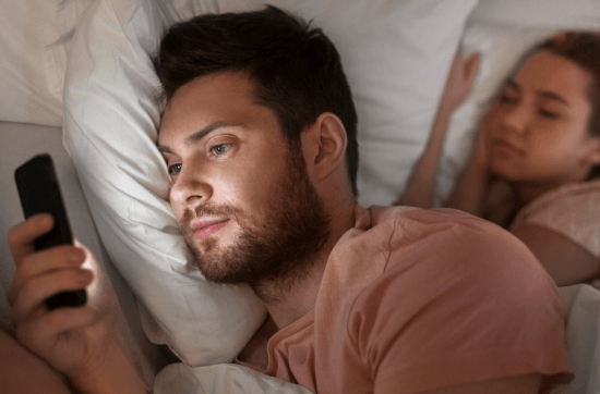 couple in bed and man looking at his mobile messages while woman sleeps