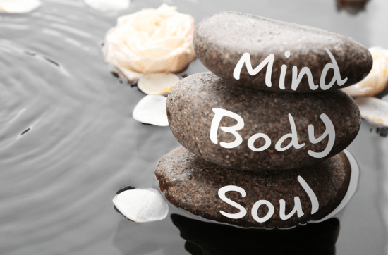 three pebbles lined up on a beach with words body, mind, soul written on it