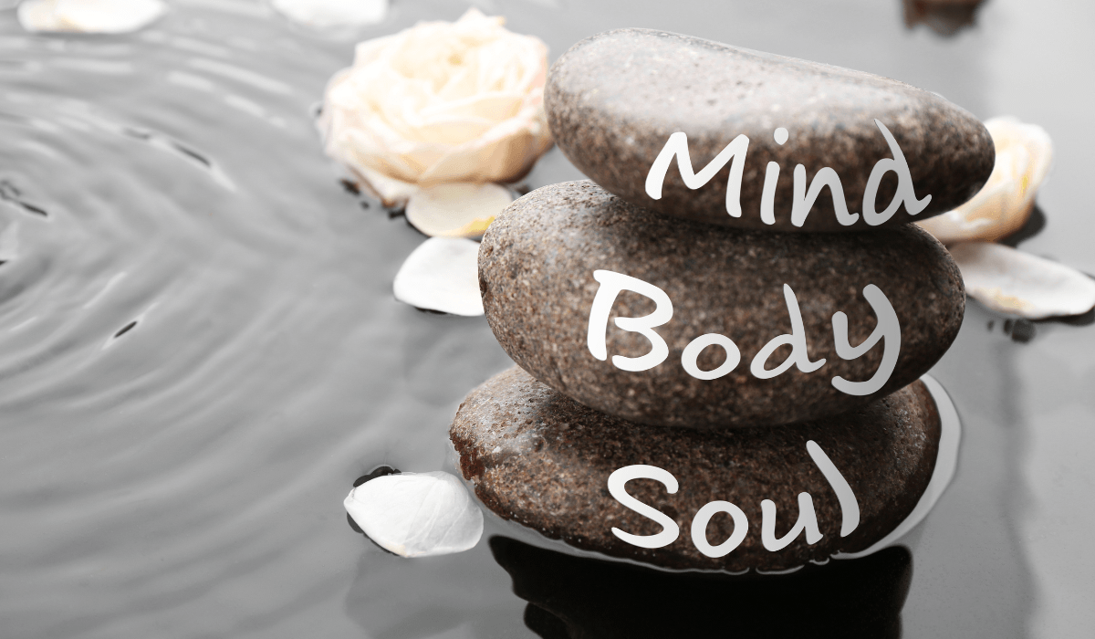 three pebbles lined up on a beach with words body, mind, soul written on it