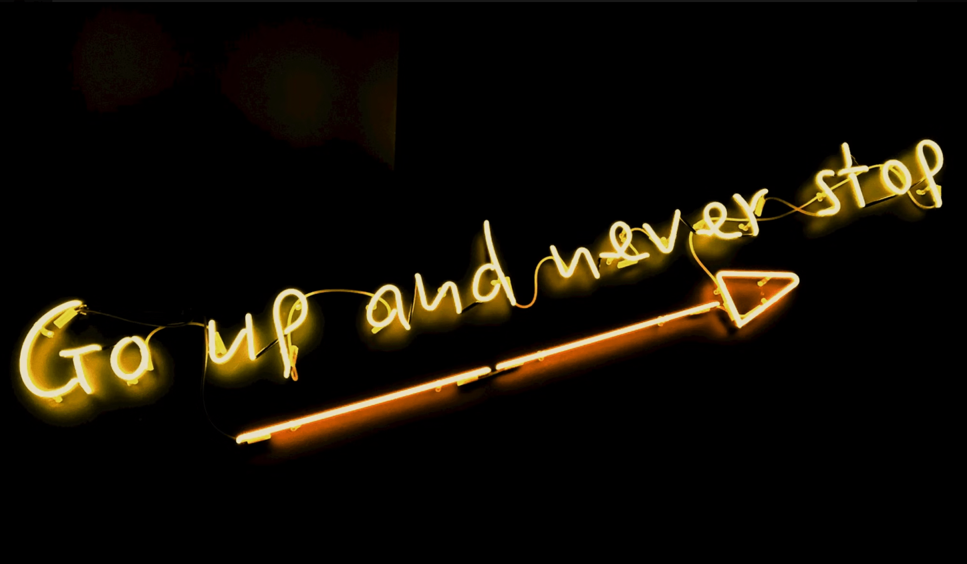 yellow neon sign on black background saying go up and never stop