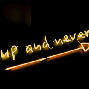 yellow neon sign on black background saying go up and never stop