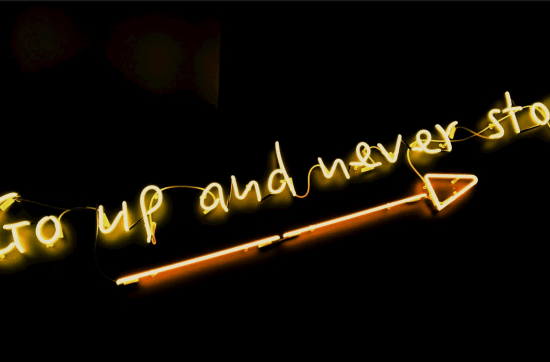 yellow neon sign on black background saying go up and never stop