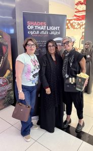 A full-length photo of Sahar with the director and the artist standing in front of a tall promotional banner for Shades of That Light at VOX Cinema Wafi Mall. Sahar is on the right holding a box of popcorn. The group poses together in a well-lit cinema foyer, with other attendees visible behind them.