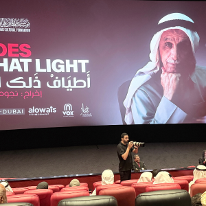 A wide-angle photograph of the cinema hall at VOX Wafi Mall during the premiere of Shades of That Light. The large screen displays the film’s title in English and Arabic, along with the portrait of Sultan Bin Ali Al Owais. The audience sits in red theatre seats, while a photographer stands near the front capturing the event. The atmosphere is attentive and formal, with Emirati attendees dressed in traditional clothing.