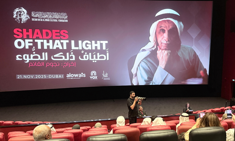 A wide-angle photograph of the cinema hall at VOX Wafi Mall during the premiere of Shades of That Light. The large screen displays the film’s title in English and Arabic, along with the portrait of Sultan Bin Ali Al Owais. The audience sits in red theatre seats, while a photographer stands near the front capturing the event. The atmosphere is attentive and formal, with Emirati attendees dressed in traditional clothing.